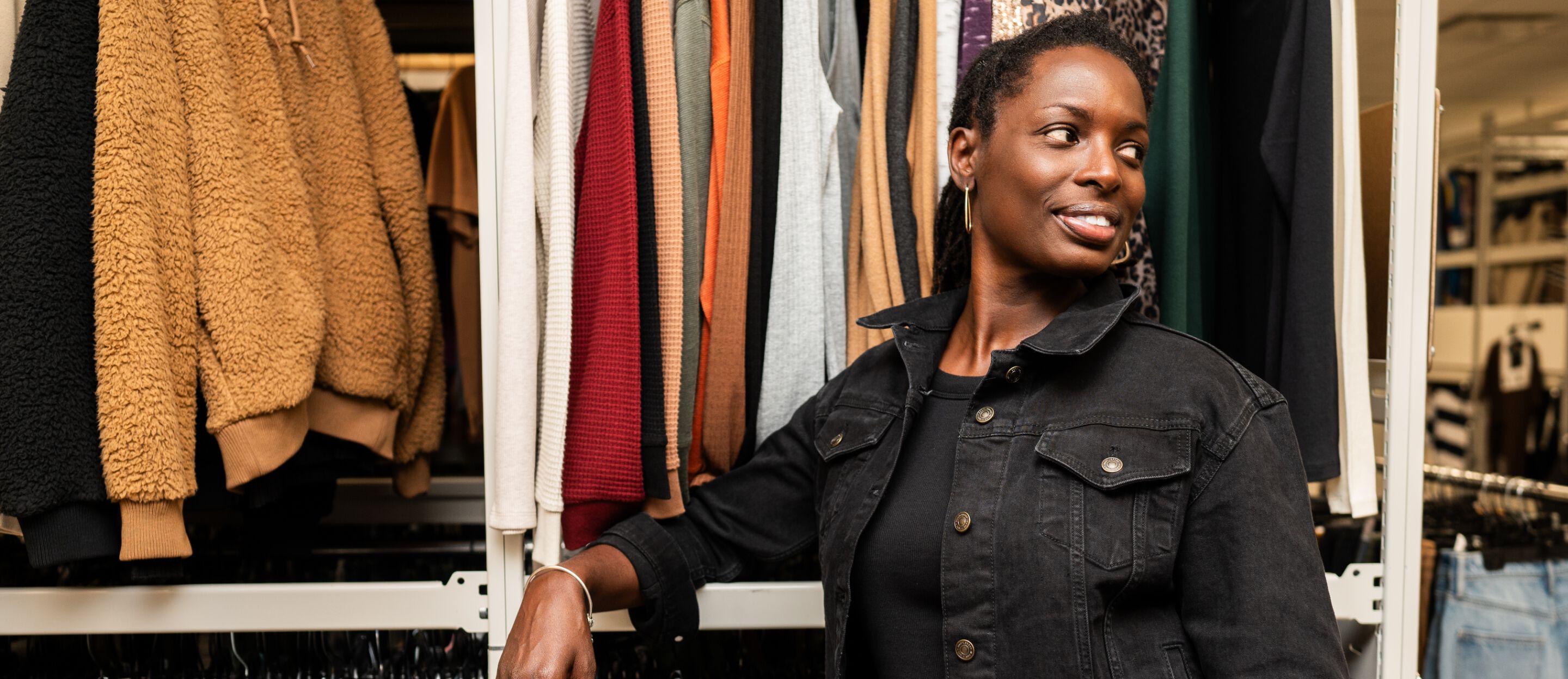 Tricia Lake leans against clothing rack wearing denim jacket.