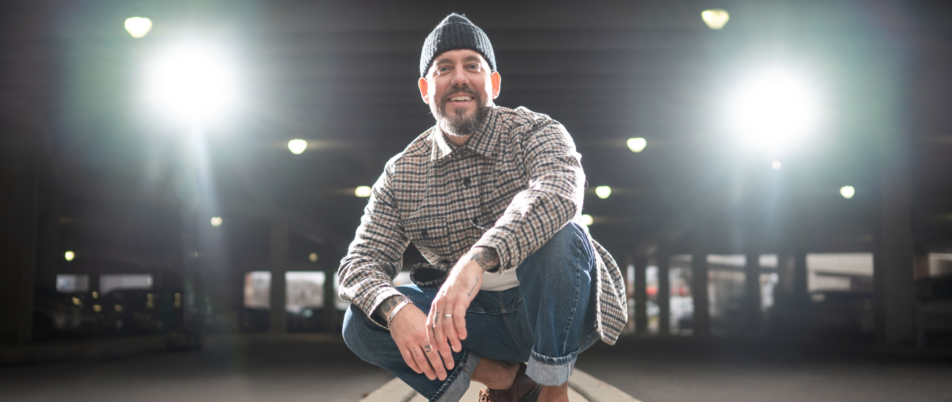 Morgan Rubio-Perez, in a beanie and a plaid button up shirt, exterior with parking background.