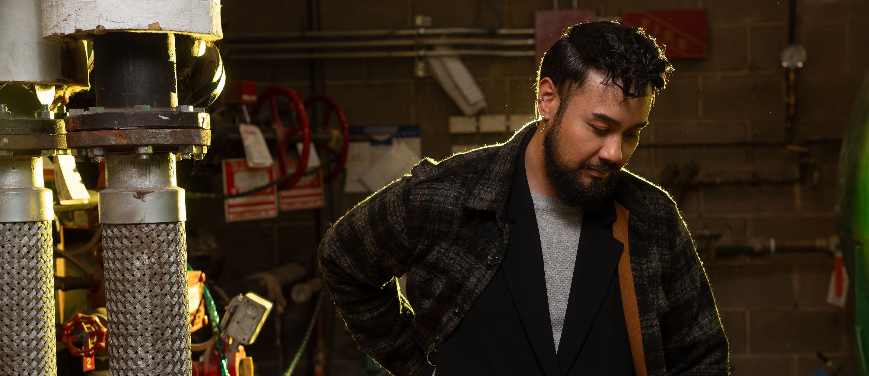 A man with a beard, Renyl Lantano, wearing a plaid standing in a boiler room.